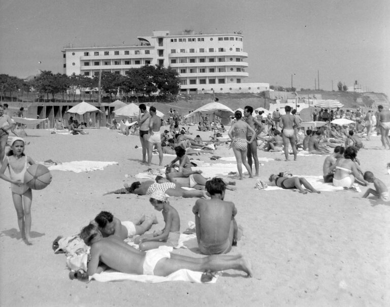 Fotografie alb-negru din 1957: plaja plină de oameni, cu hotelul alb sus, pe faleză