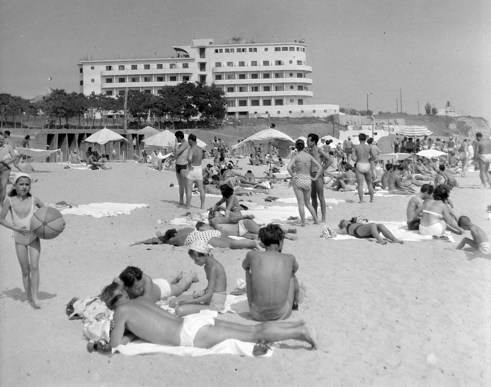 Fotografie alb-negru din 1957: plaja plină de oameni, cu hotelul alb sus, pe faleză