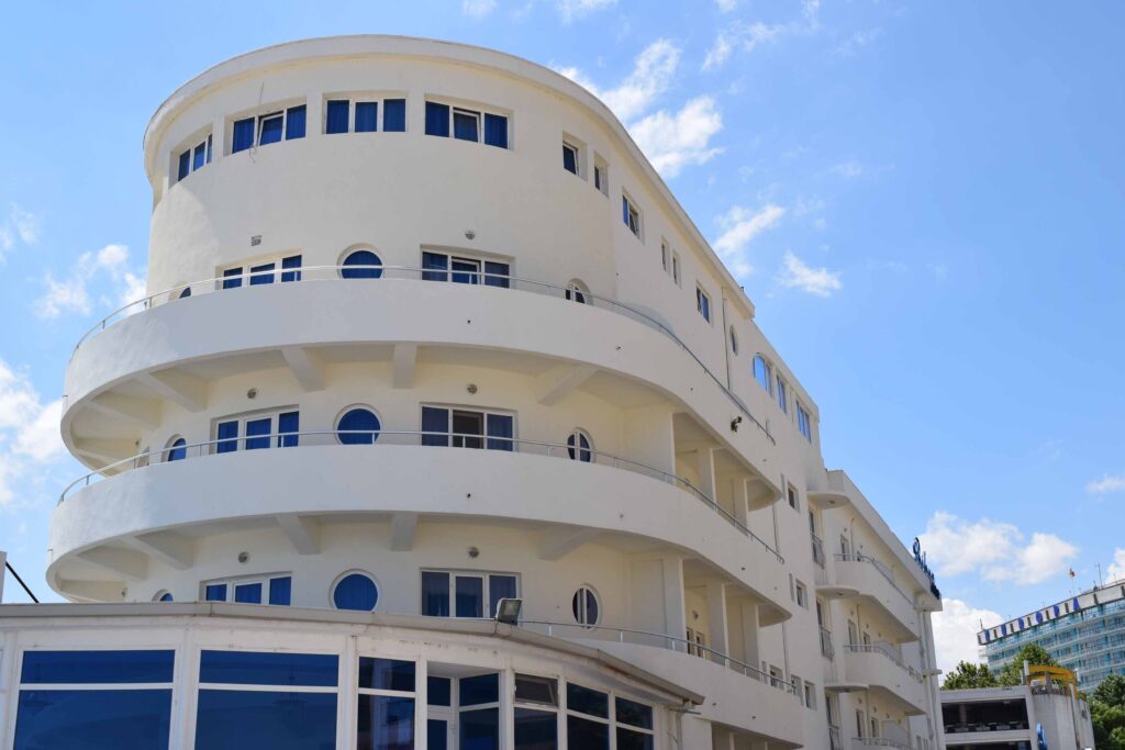 Prova rotunjită și albă a Hotelului Belona, cu balcoane curbe și ferestre rotunde, pe cer albastru