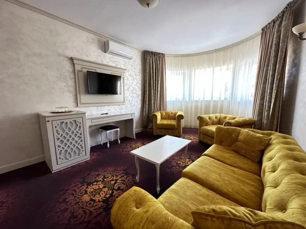 Livingul Apartamentului Belona, cu canapea galbenă și ferestre pe peretele curb