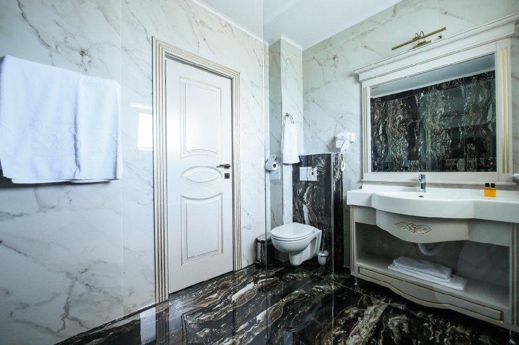 Baie la Hotel Belona, cu pereți de marmură albă și lavoar cu oglindă
