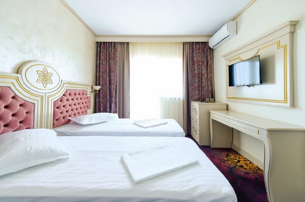 Cameră twin la Hotel Belona, cu birou, televizor și mobilier alb cu auriu