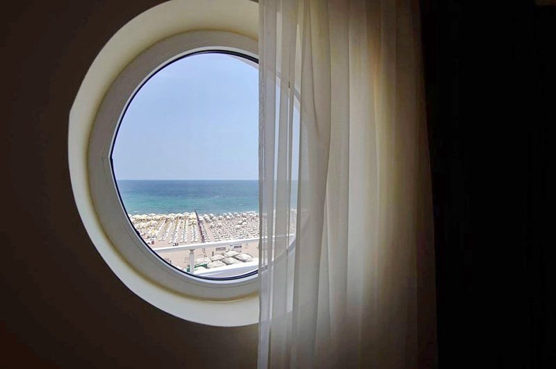 Fereastră rotundă, ca un hublou, la Hotel Belona, cu vedere spre plajă și mare
